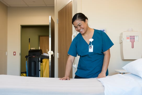 An HHS EVS team member smiling while making a hospital bed, demonstrating a clean, welcoming environment that promotes positive patient experiences.