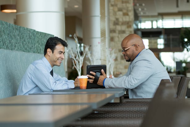 Two businessmen discuss data displayed on a tablet