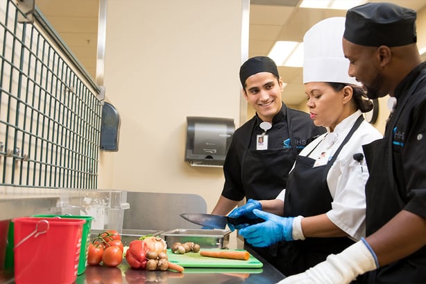 Female chef teaching cooks inside hospital kitchen
